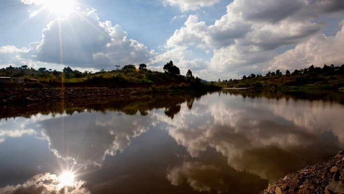 Sonne und Wolken spiegeln sich auf einer Flußlandschaft