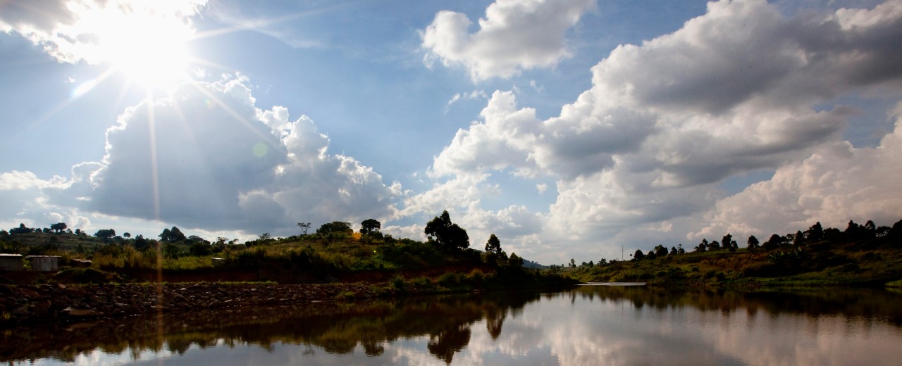 Sonne und Wolken spiegeln sich auf einer Flußlandschaft