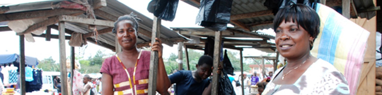 Zwei Marktverkäuferinnen in Ghana stehen vor ihrem Stand und verkaufen Maniok