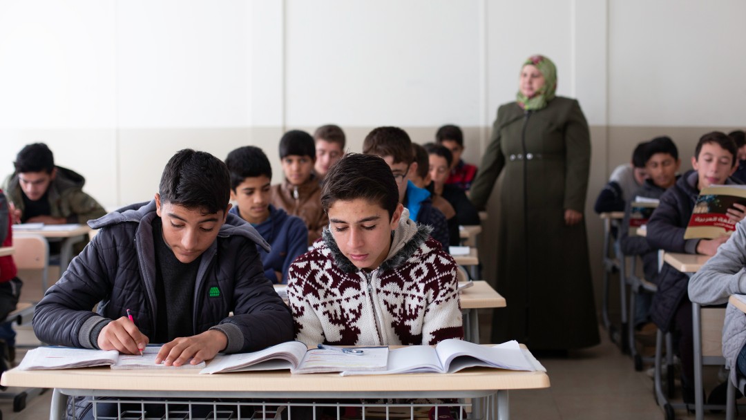 In a classroom, students read a text while the teacher is watching them.