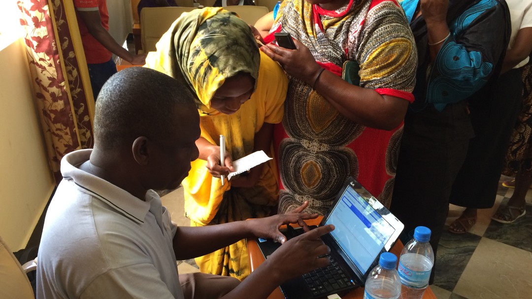 Women queue up to be shown the digital solutions on a computer.