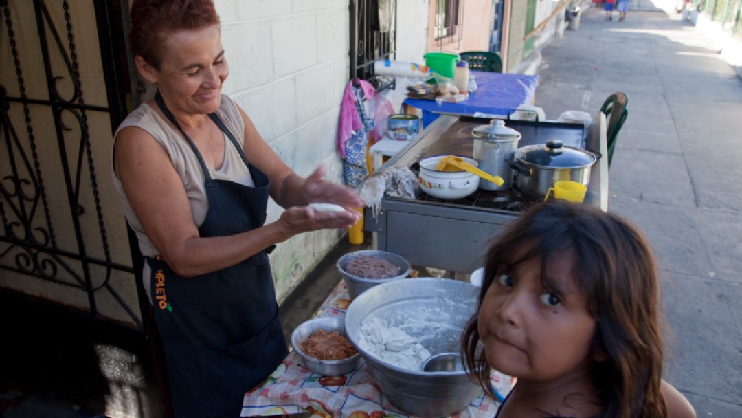 young girl in front of the picture watching an older woman cooking in the backround 