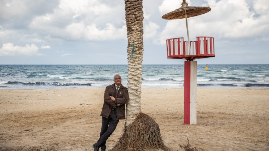 Engineer Mohammed Ali Torki stands on the beach, leaning against a palm