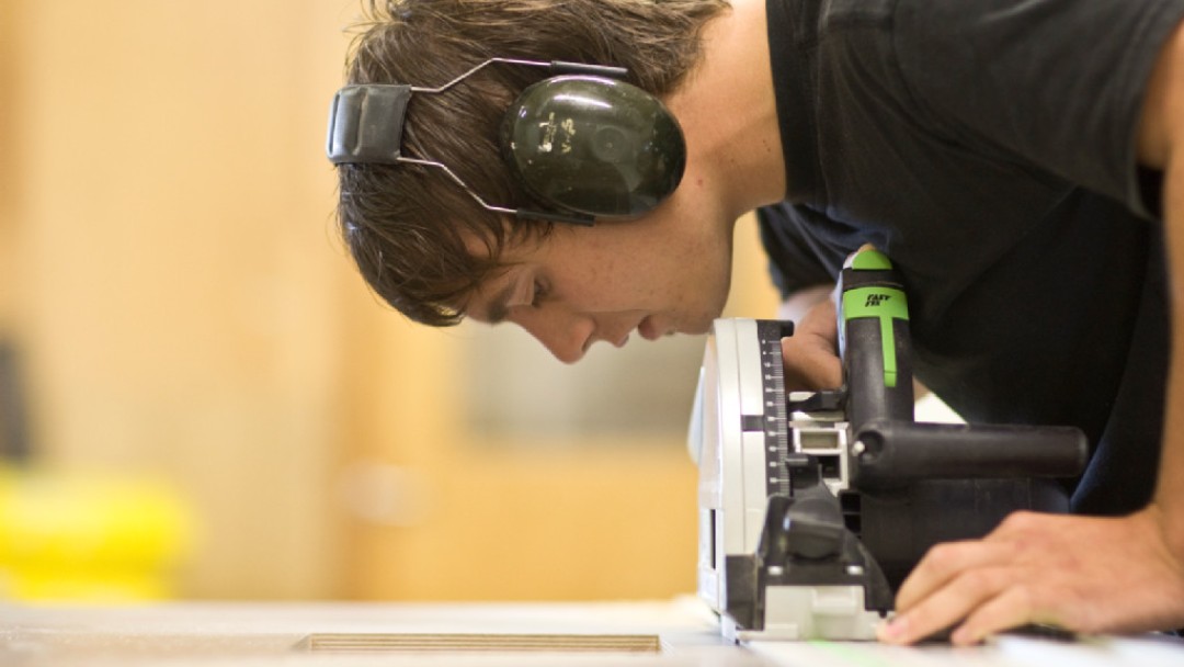 A young man wearing sonic headphones is working on a grinding machine