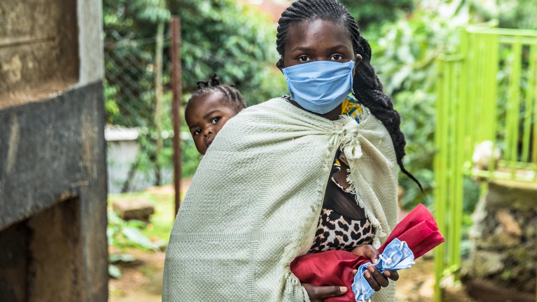 Kenyan woman with face mask wearing her child