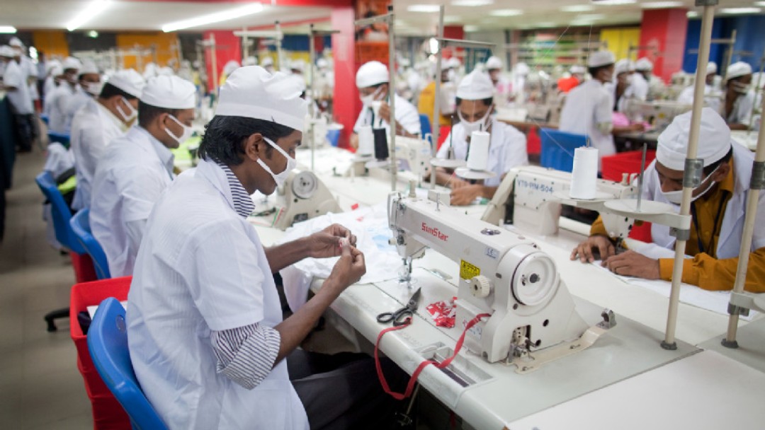 Workers in a textile factory sit at sewing machines and make garments.