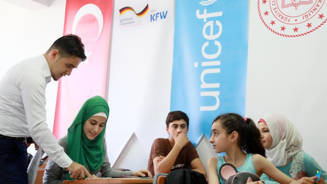 A teacher helps four Syrian refugee children in Turkey with their schoolwork.