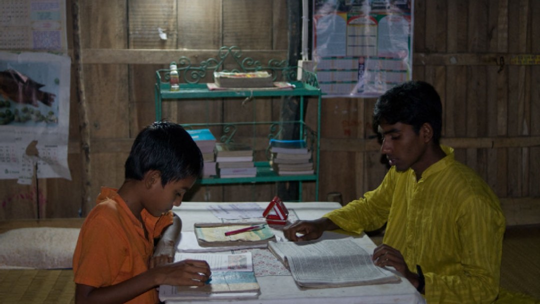 Kind und Jugendlicher erledigen Hausaufgaben bei künstlichem Licht.