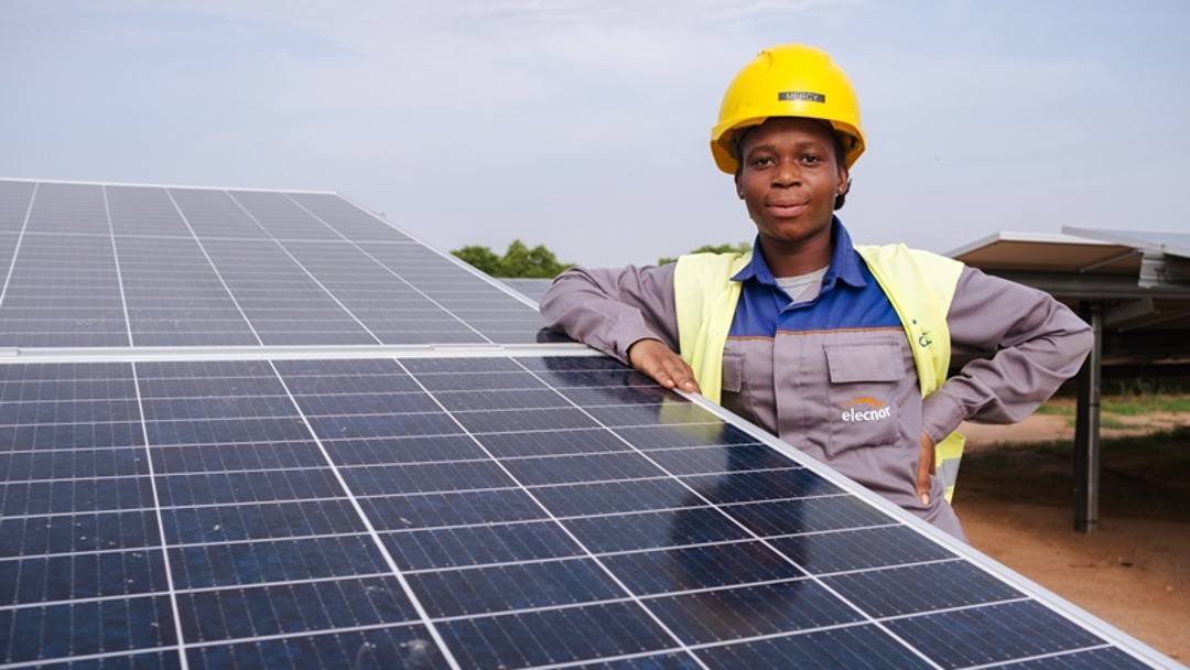 Eine Solartechnikerin steht an einer großen Solaranlage in Ghana 