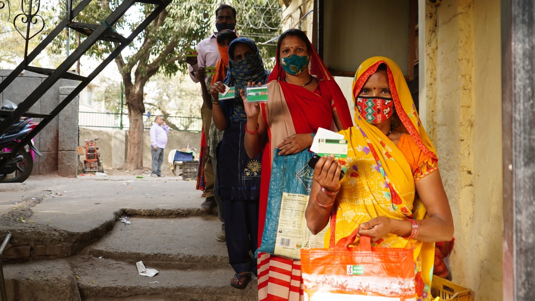 Bewohnerinnen eines Armenviertels in Delhi warten vor einen Lebensmittelgeschäft
