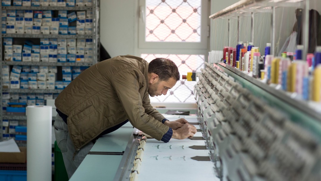 Employees of an embroidery company working on an embroidery machine.