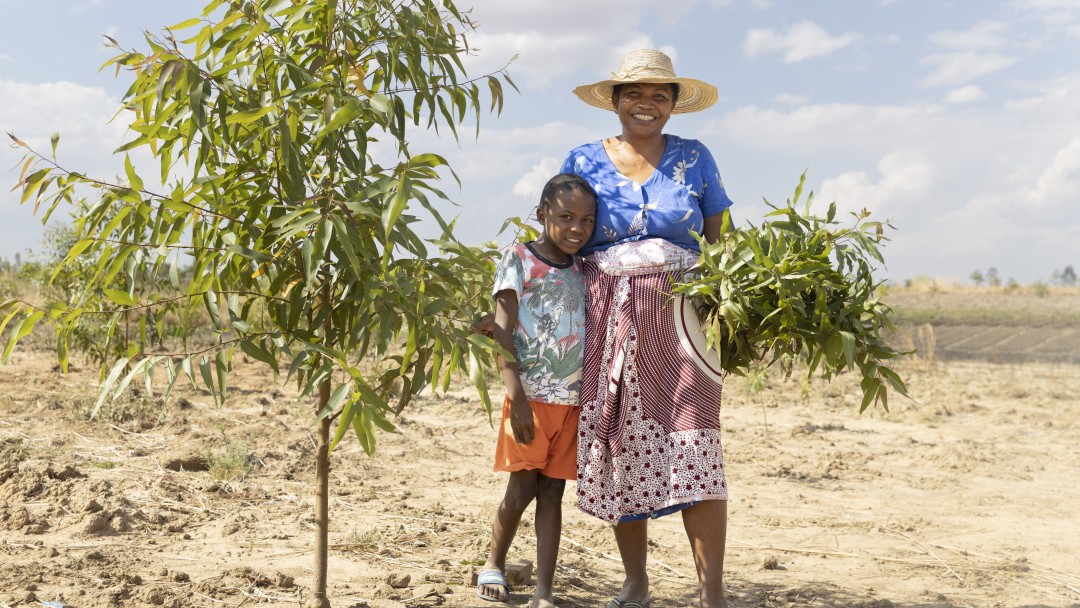 Eine Frau mit ihrem Sohn steht neben einem Baum lächelnd. 