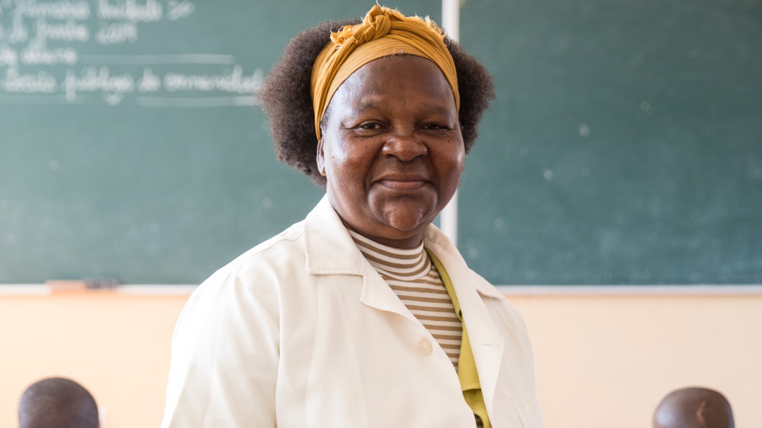 A teacher with a white shirt standing in front of her classroom. 