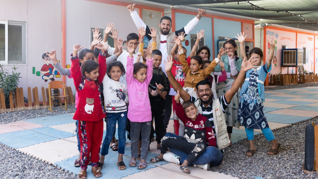 Mehrere Kinder im Jedah-Flüchtlingslager strecken die Hände in die Luft, dazwischen zwei Betreuer