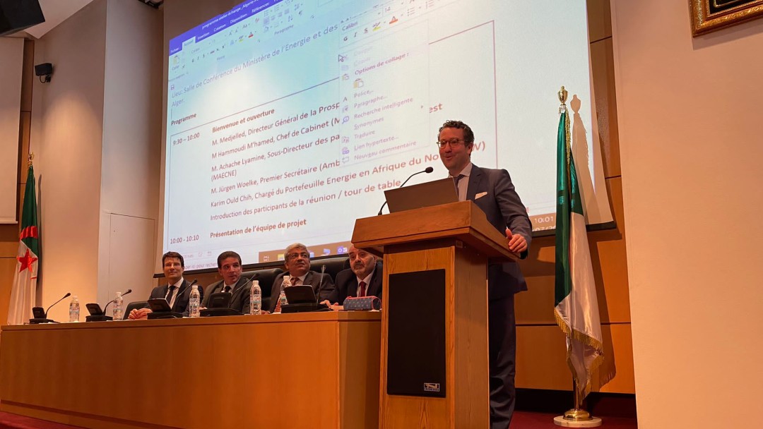 A man held a speech on stage next to a flag and four other colleagues