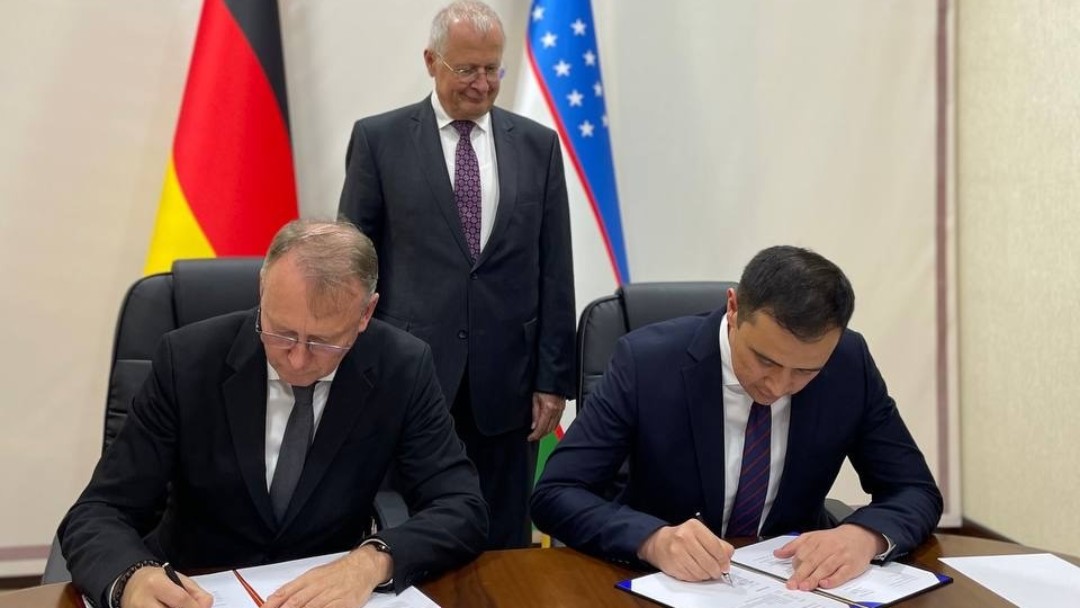 Two men signing an agreement with another colleague standing in the background