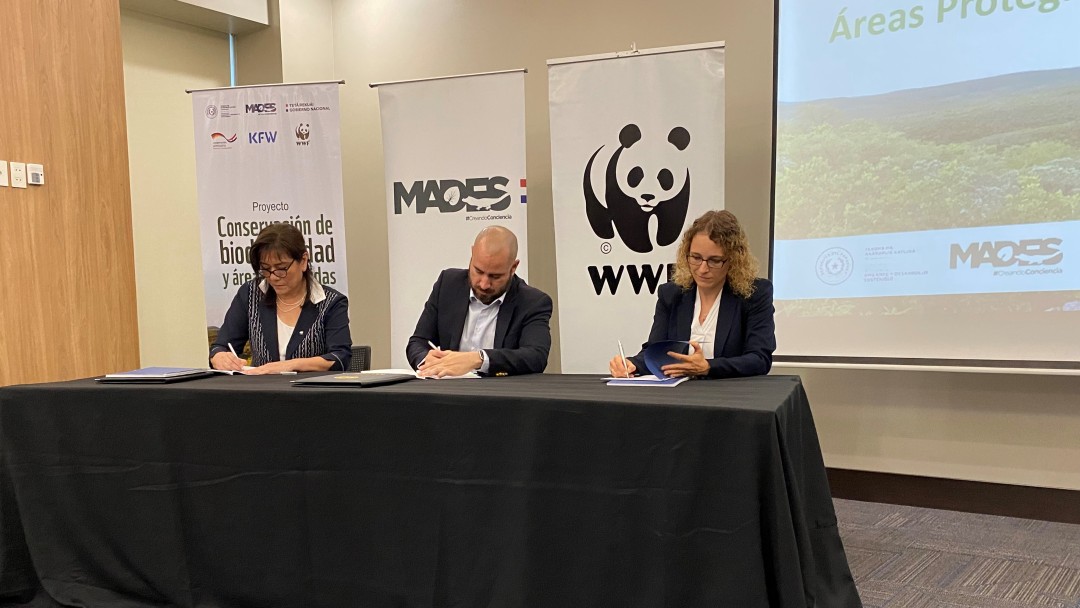 Three people sitting down on a table signing a paper