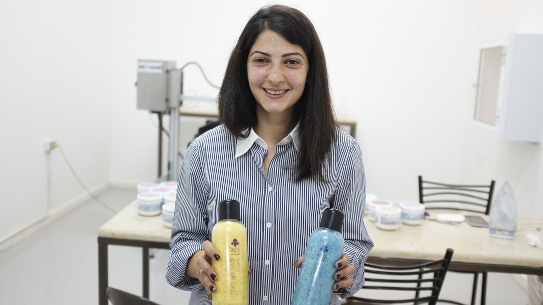 Eine Frau lächelt und hält zwei Flaschen Kosmetikartikel in ihrer Hand. 