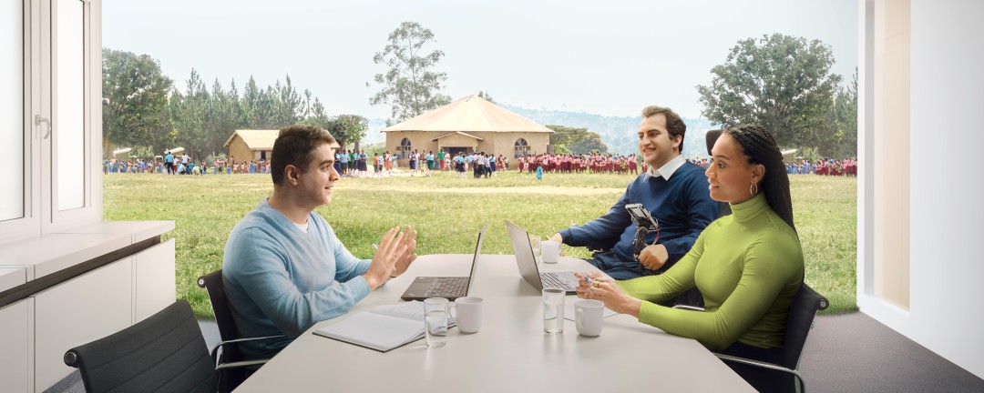 3 Personen an einem Tisch, Schule mit Schulkindern im Hintergrund