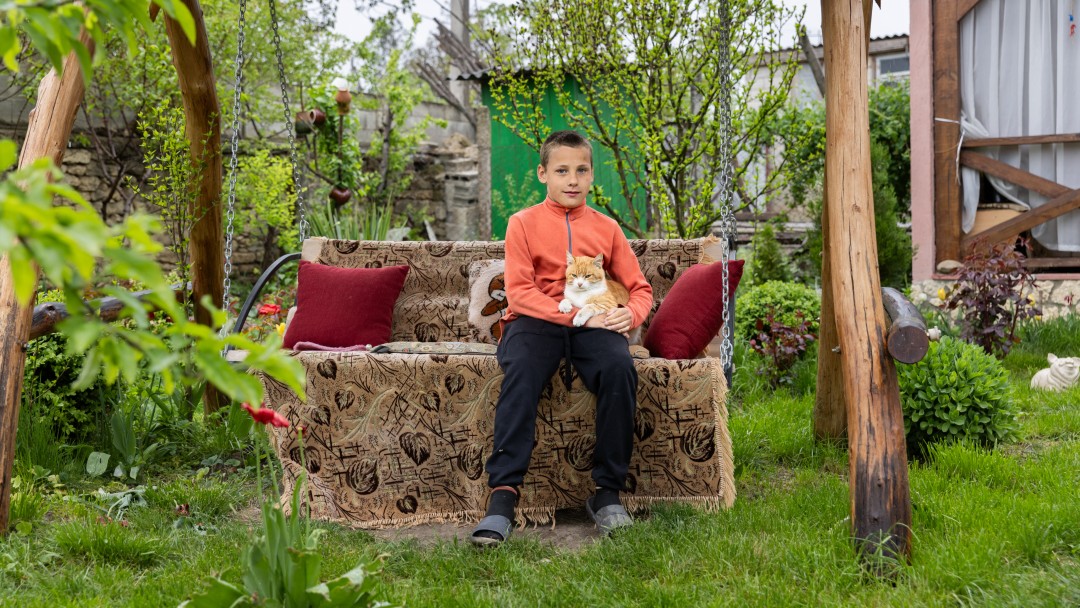 A boy sits with a cat on a wooden swing