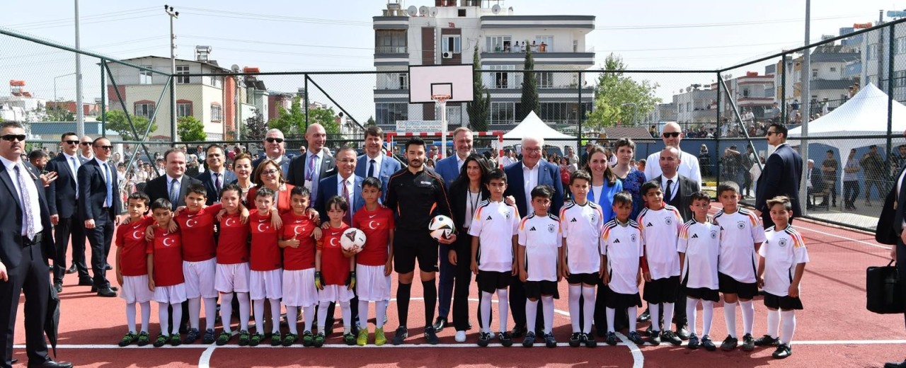 Bundespräsident Frank-Walther Steinmeier steht für ein Gruppenfoto auf einem Fußballplatz. Kinder tragen Trikots der deutschen und türkischen Fußball-Nationalmannschaften 