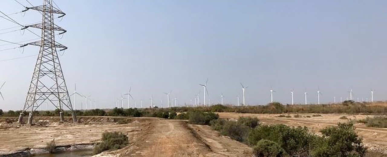 Unbefestigte Straße mit Umspannturm sowie Windrädern am Horizont