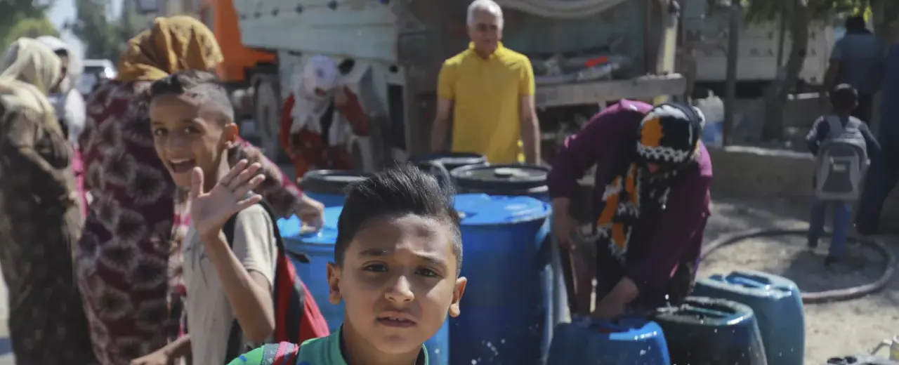 Kids and Adults filling water into barrels 