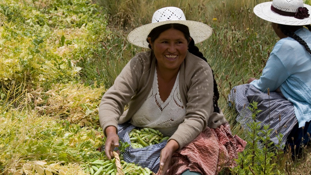 A woman is sorting beans in a field, she smiles into the camera