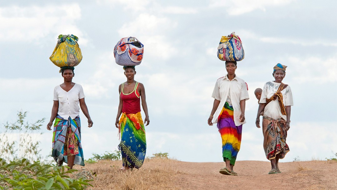 Frauen transportieren in Tücher gewickelte Waren auf ihren Köpfen zu einem Markt.