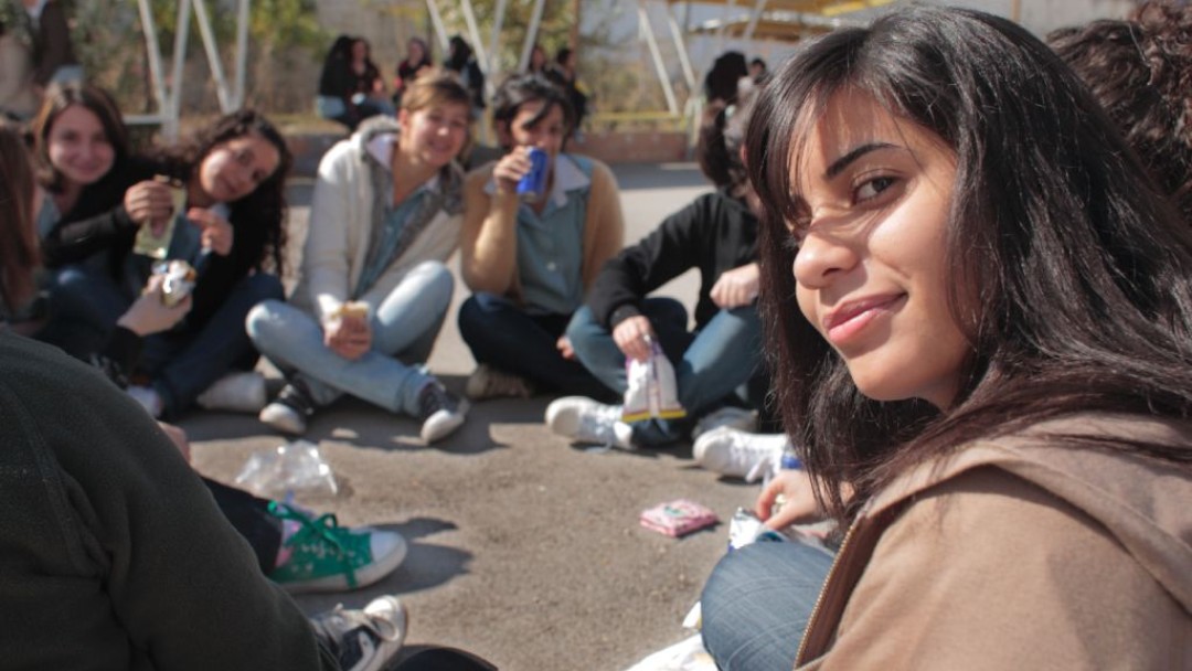 A group of female students sitting on the ground, one girl is turning around and smiling into the camera