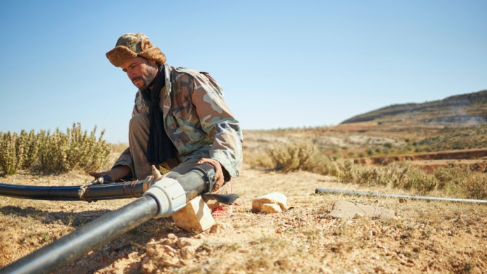A man checks the connection of pipes that supply water to farmland.