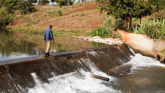 An African man walks across a small dam that dams up the water of a river.