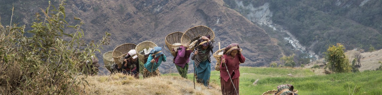 Women carry baskets up a steep hill 