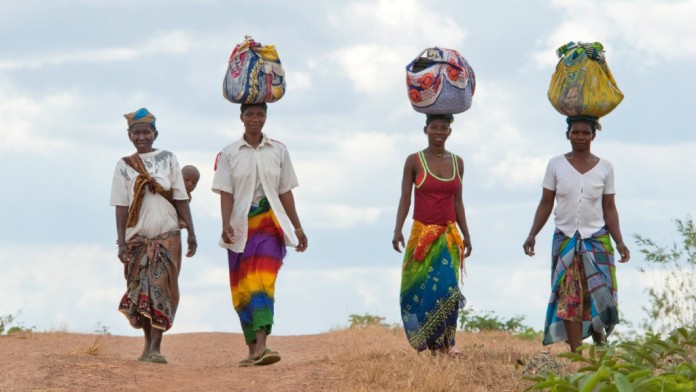 Vier Afrikanerinnen tragen Lasten auf dem Kopf.