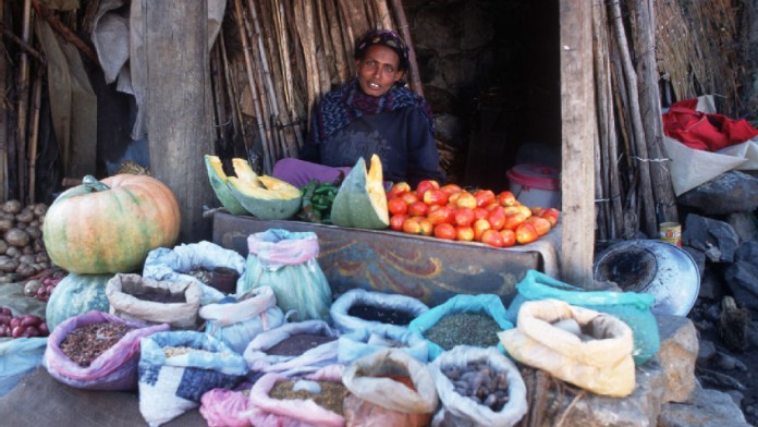 Eine Frau mit diversen pflänzlichen Lebensmitteln auf ihrem Marktstand