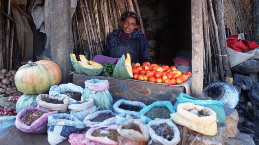 Eine Frau mit diversen pflänzlichen Lebensmitteln auf ihrem Marktstand