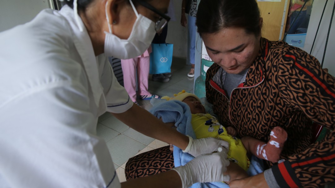 Doctor vaccinates baby lying on the lap of its mother