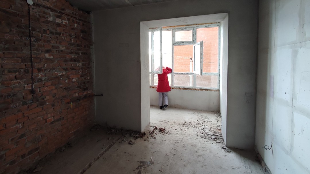 Eine Person steht in einem wiederaufgebautem Haus und schaut aus dem Fenster 