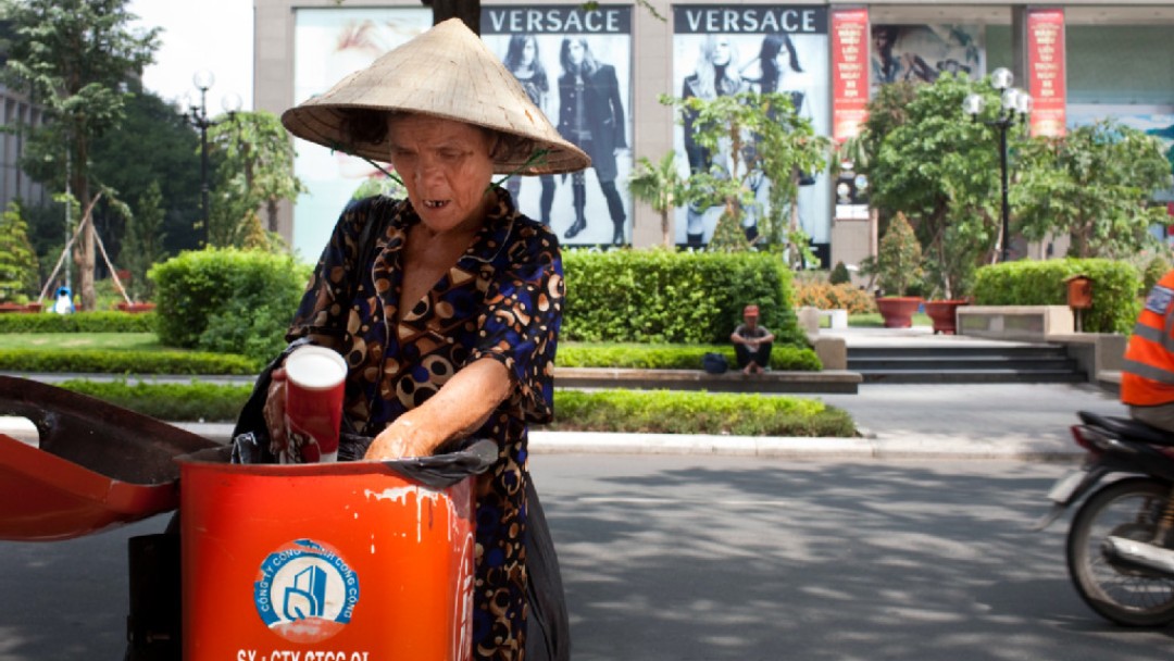 Woman with hat rummages in garbage, Versace in background