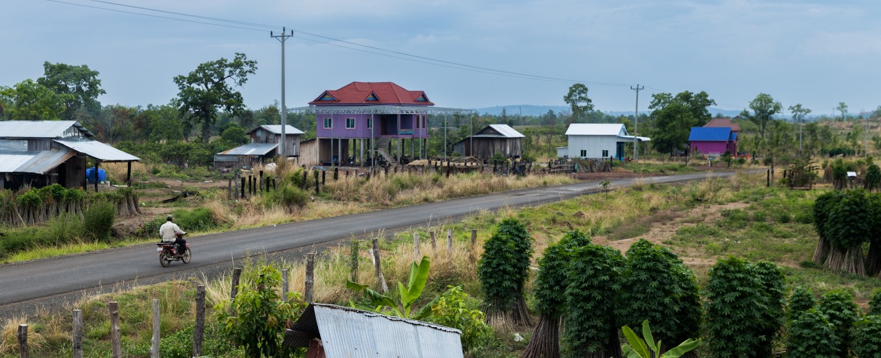 A scooter crosses a street, behind it houses