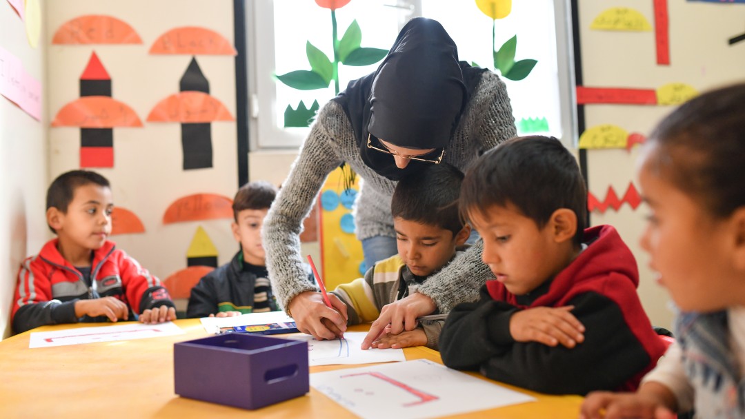 Several children at a table, a teacher helps one of the children