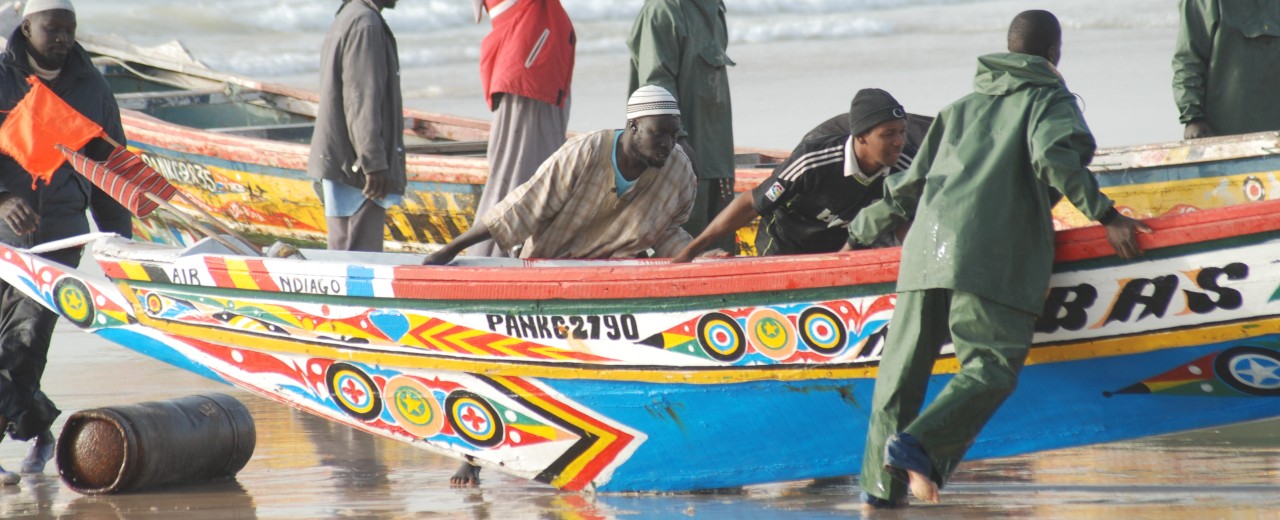 Fischer schieben ein Boot mit Ornamenten ins Wasser