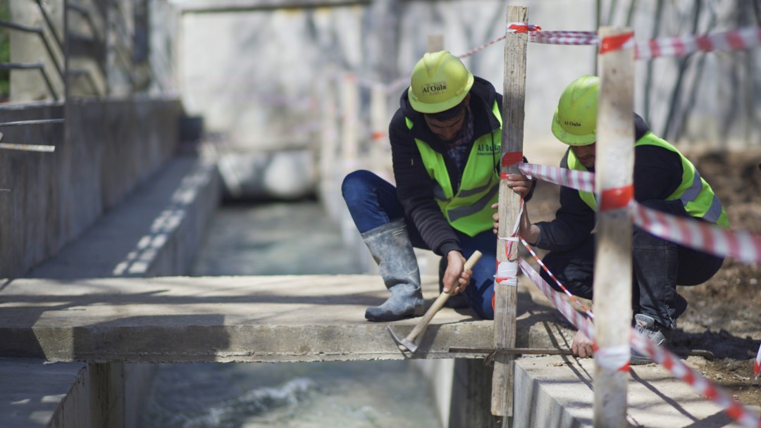 2 Studenten des WASH-Programms in Arbeitskleidung und -helm arbeiten an einer Baustelle