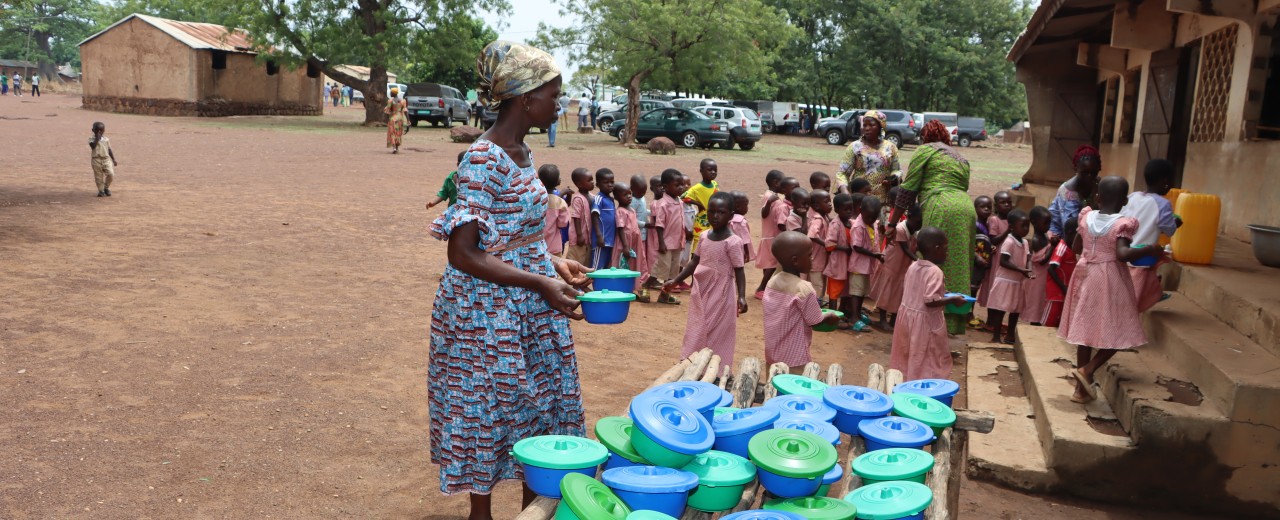 A woman with bowls and schoolchildren in front of a building