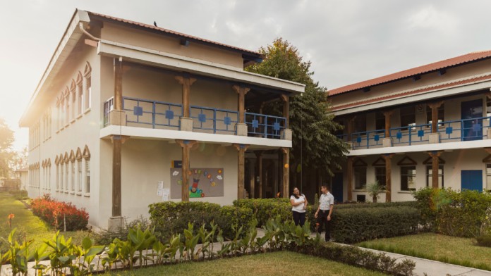 Zwei Studierende in einer Grünanlage vor einem zweistöckigen Universitätsgebäude