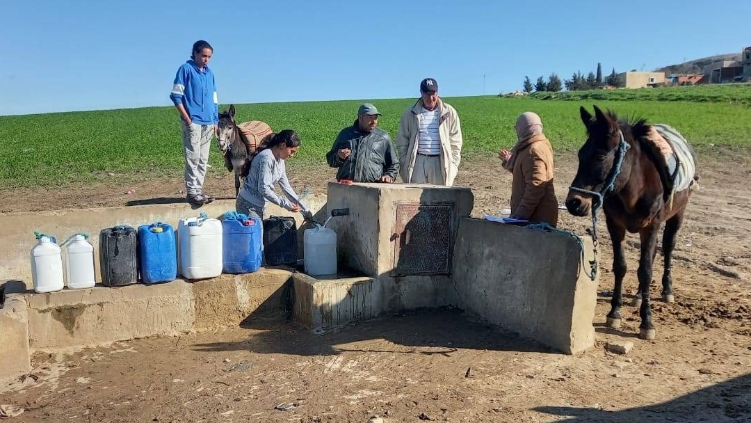 Fünf Personen füllen Wasserkanister an einer Quelle auf.