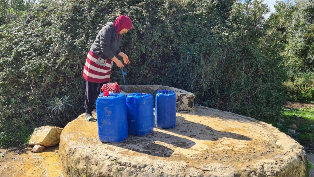 Frau mit Wasserkanistern an einem Brunnen