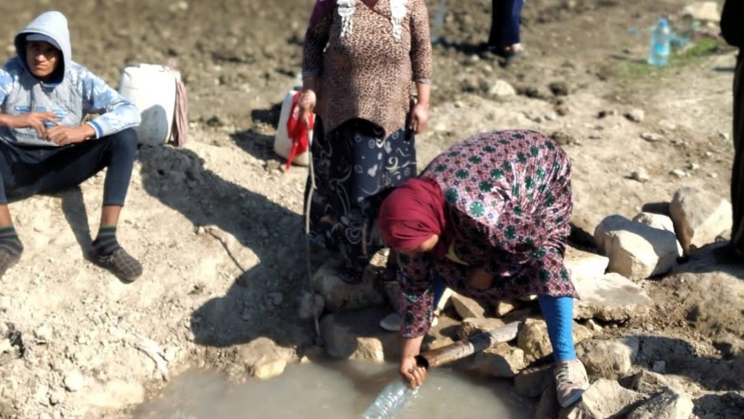 Zwei Frauen füllen Wasserflaschen an einer Quelle auf.