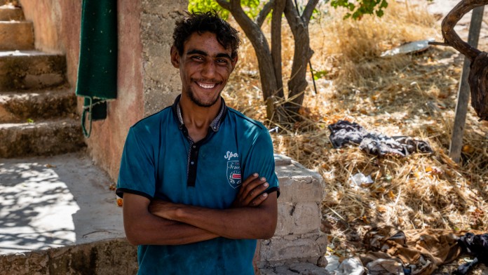 Mahmoud Al Abed stands outside a wall and smiles