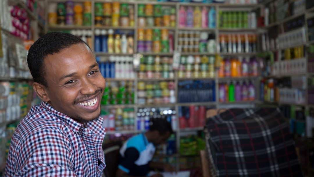 Leban Tahlil stands in a small store in the Kakuma refugee camp and smiles into the camera. 